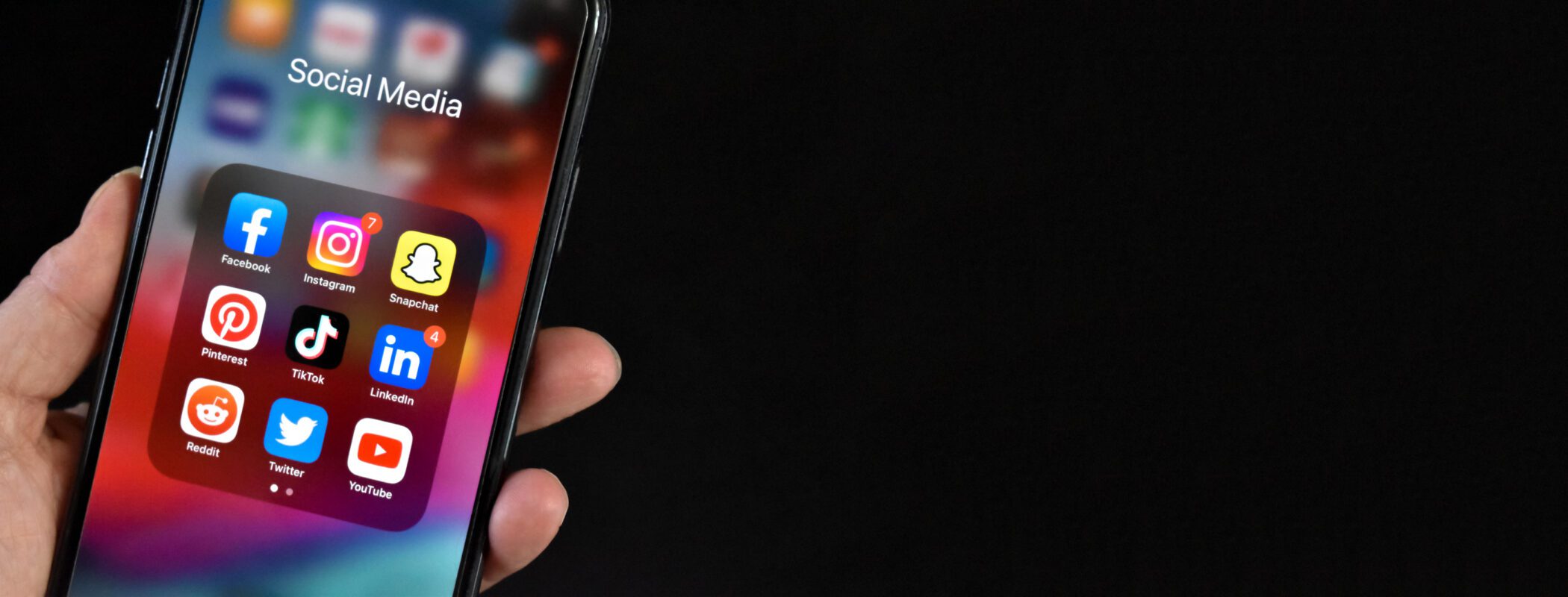 hand-holding-cell-phone-with-social-media-apps-on-screen-smartphone-mobile-online-application-icons-over-black-background-with-copy-space-panoramic