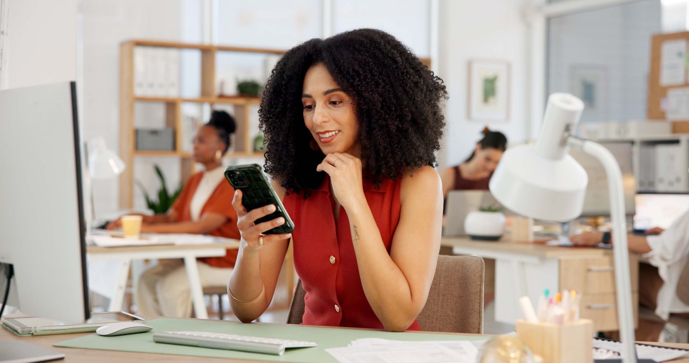 happy-woman-and-typing-in-creative-agency-with-phone-computer-and-trend-for-social-media-marketing-person-coworking-and-tech-in-office-for-campaign-post-online-brand-awareness-and-advertising